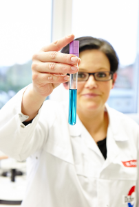Eine Mitarbeiterin von Dr. Suwelack hält ein Reagenzglas mit blauer Flüssigkeit in die Kamera.